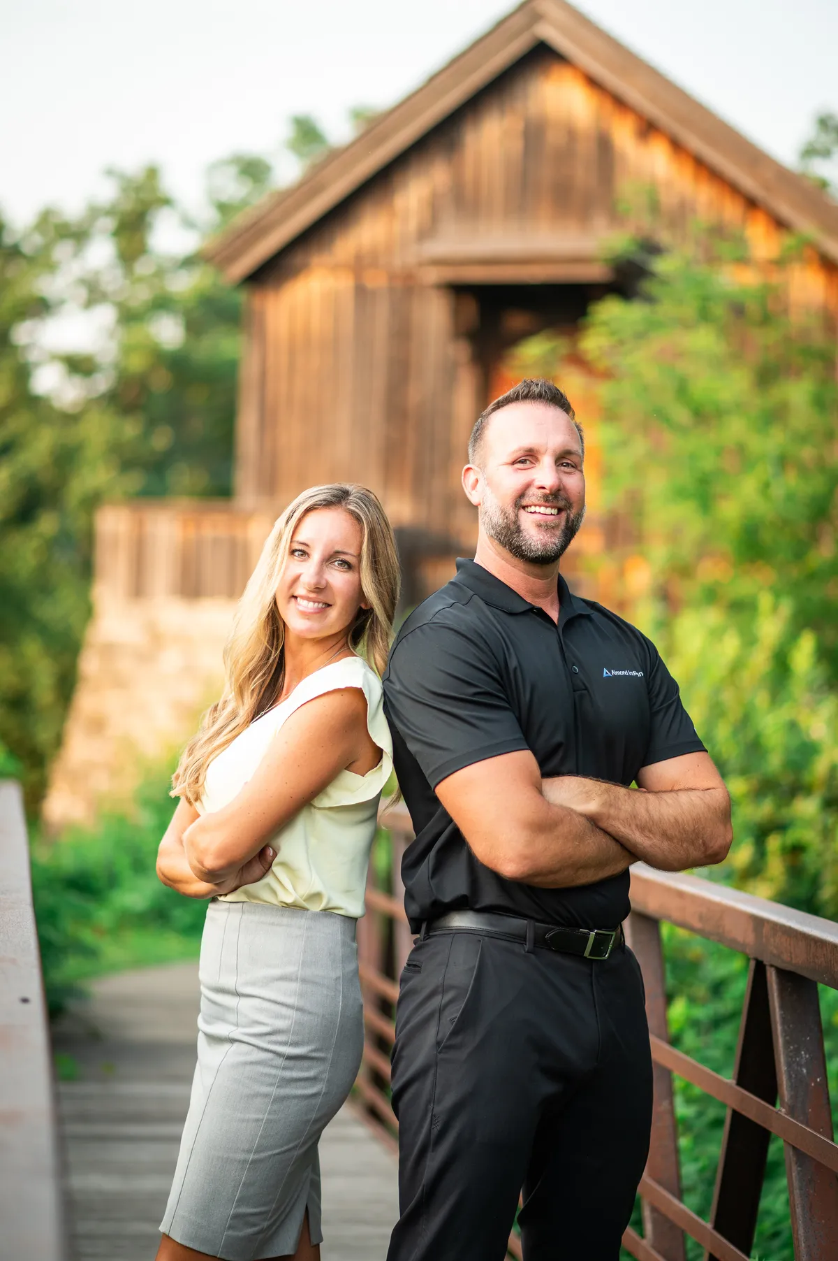 Joe and Serenity Almond, co-founders of Almond Insurance, standing back-to-back on an outdoor bridge in Rockford, IL